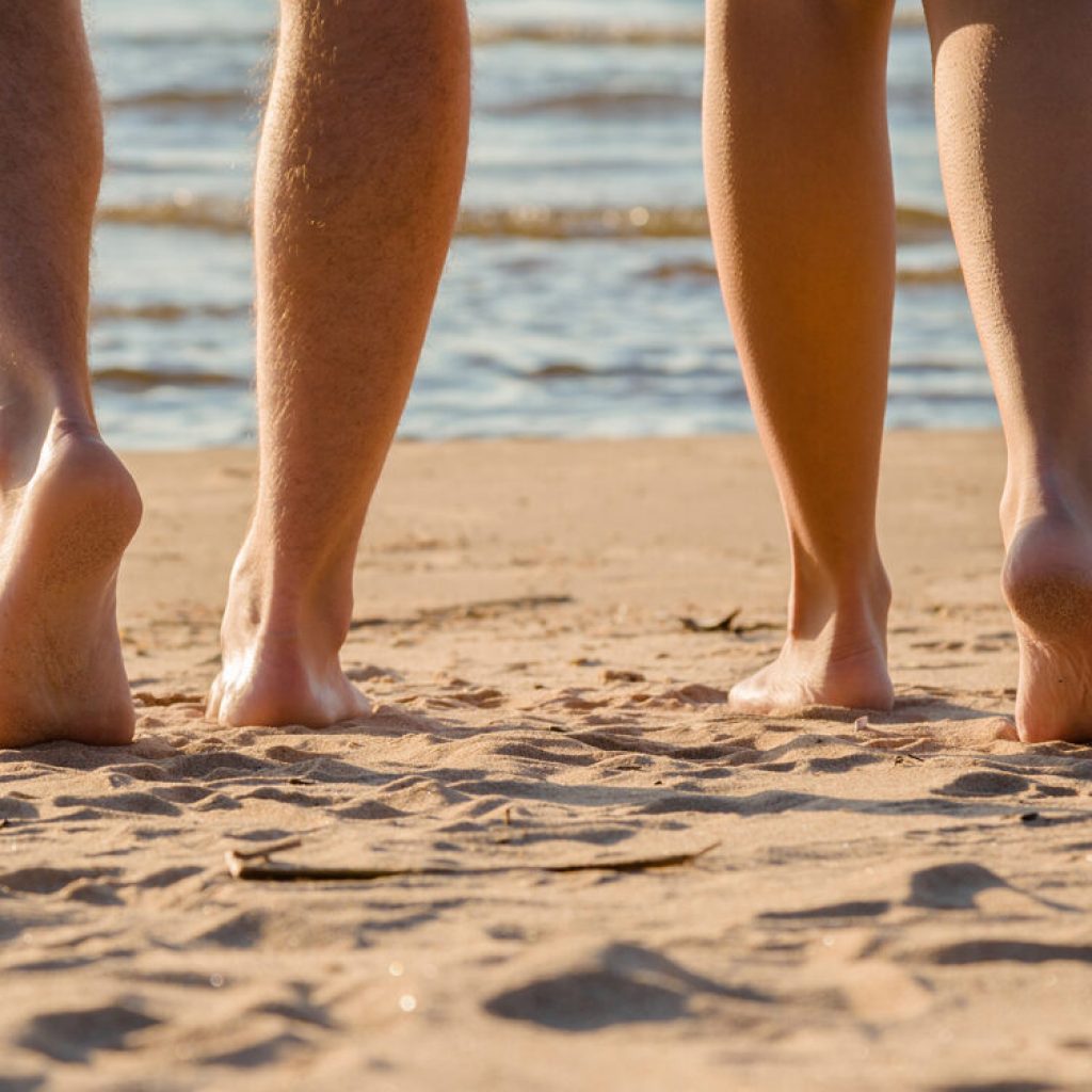 Young couple's barefoot going to swim in cold sunny day. Woman legs have goosebumps. Back view. Closeup.